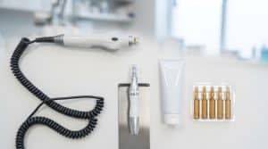 Beyaz zeminde çatlak tedavisi araçlarının düz yerleşimi: fraksiyonel lazer başlığı, microneedling kalemi, etiketsiz dermatoloji kremi ve serum ampulleri