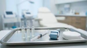 Çelik tepside dizilmiş ince mezoterapi serum ampulleri, kapaklı narin enjektör, soğutucu roller ve pamuk, dermatoloji tedavi odası