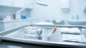 Steril tepside kapaklı ince enjektör yanında etiketsiz botulinum toksin flakonu, modern dermatoloji odası arka planı